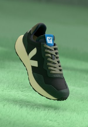 Zapatillas negras y verde oscuro con parte superior texturizada, suela beige y cordones verde claro. Presentan una etiqueta azul con el logo "VEJA".