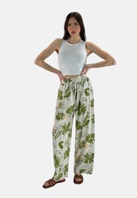Witte crop top, bloemenpatroon wijd-uitlopende broek in pastelgroen en beige, en bruine sandalen. De broek heeft een elastische tailleband met trekkoord.