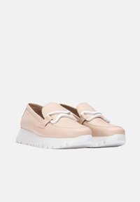 Zapatos de slip-on de cuero beige con punta redondeada, cordones blancos de acento y una suela de goma blanca con un dibujo texturizado.