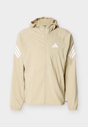 Beige letvægtsjakke med hætte, fuld lynlås, elastiske manchetter og hvidt trekantet logo samt striber på ærmerne.