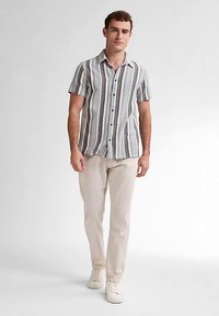 Kortärmad skjorta med knappar i blå och beige ränder, med spridningkrage och avslappnad passform. Kombinerad med byxor i krämfärg och vita sneakers.