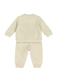 Survêtement en coton beige comprenant un haut à manches longues avec des poignets côtelés et un pantalon assorti au design simple. Sans motifs ni accents.