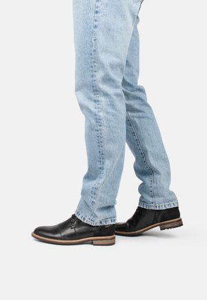 Zapatos de cuero negro con un acabado suave, tacón bajo y detalles de cordones, combinados con jeans de mezclilla azul claro.