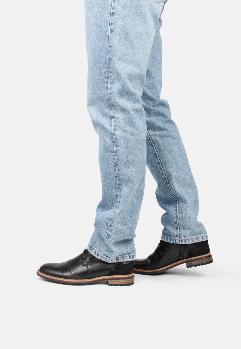 Zapatos de cuero negro con un acabado suave, tacón bajo y detalles de cordones, combinados con jeans de mezclilla azul claro.