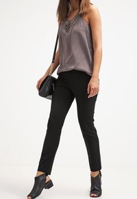 Grå satin camisole med spetsdetaljer, parat med svarta smalpassande byxor och svarta öppna klackskor med blockklack. Accentuerad med en liten väska.