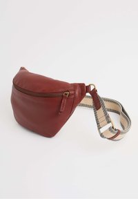 Raudona odinė fanny pack'ą su tekstūruotu paviršiumi, auksine užtrauktuko diafragma ir kremine bei juoda juostele, reguliuojama ilgio. Kompaktiškos, apvalios formos.