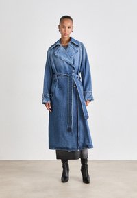 Lange spijkerjas in lichtblauw, met een dubbelbreasted ontwerp, brede kraag, tailleband en zijzakken. Glad textuur en tot de knie.
