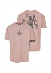 Camiseta de algodón rosa claro con mangas cortas. En la parte frontal tiene el texto "inocente hasta que se demuestre lo contrario". En la parte posterior muestra un gráfico de la Dama Justicia y palomas.