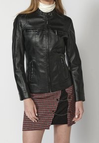 Czarna skórzana kurtka o dopasowanym kroju, z dwoma zamykanymi na zamek kieszeniami na piersi, kieszeniami bocznymi oraz prążkowanym wykończeniem na ramionach. W zestawie z kratowaną spódnicą.
