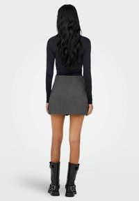 Mini-jupe plissée grise avec un ourlet droit, associée à un top noir à manches longues et des bottes noires montant jusqu'au genou avec des boucles.