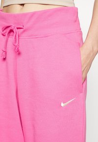 Rosa Nike sweatpants har en ribbad midja med dragsnöre, sidofickor och en liten vit Nike-logotyp på framsidan.