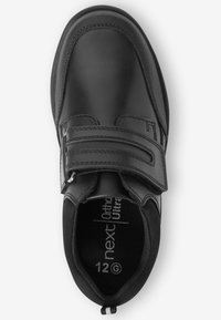 Chaussure en cuir noir avec un bout arrondi, une sangle Velcro, un col rembourré et des accents texturés. L'intérieur présente une semelle intérieure rembourrée.