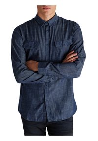 Ciemnoniebieska koszula na guziki z fakturowanej tkaniny, z długimi rękawami, kołnierzykiem i dwoma kieszeniami na piersi. Zaprojektowana z myślą o dopasowanym kroju.