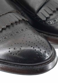 Scarpe di pelle nere con dettagli a nappe, traforature e punta arrotondata. Presentano una finitura lucida e una texture morbida.
