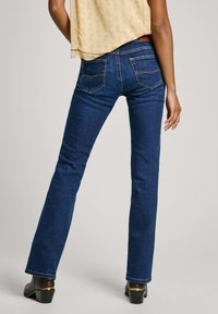 Jeans de color azul oscuro con una cintura ajustada, piernas acampanadas y bolsillos traseros contorneados con costura en contraste. La tela es de denim suave.
