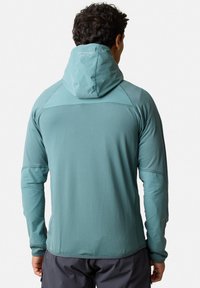 Türkiser Langarmjacke mit einer angepassten Kapuze, strukturiertem Stoff und flachen Nähten. Besitzt ein Logo auf der Kapuze und kontrastierende Ärmel.