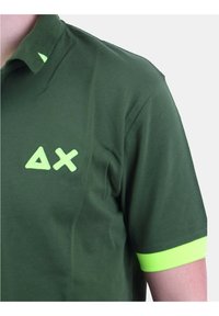 Polo verde con tessuto testurizzato, maniche corte con dettagli giallo brillante e logo verde chiaro sulla parte sinistra del petto.
