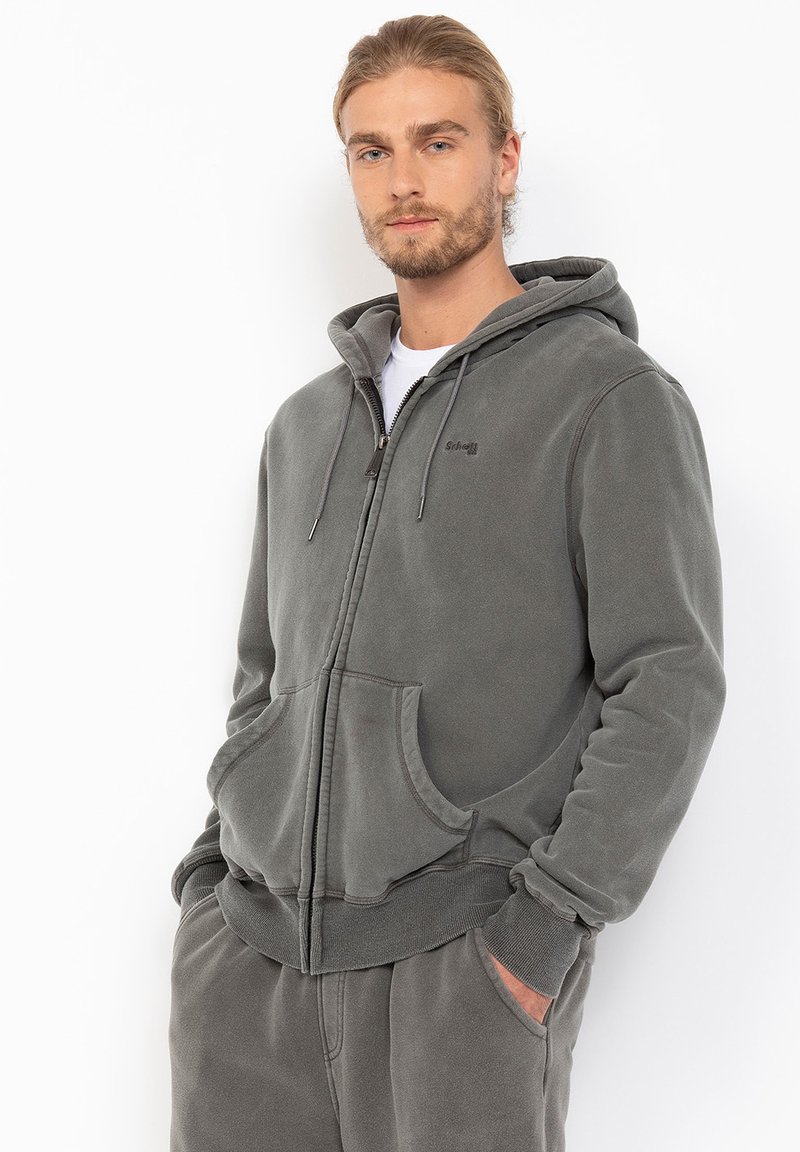 Grå zip-up hættetrøje lavet af blødt stof, med snøre i hætten, store frontlommer og ribbede manchetter. Glat tekstur med minimal branding.