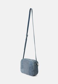 Denim torbica preko ramena s pravokutnim oblikom, svijetloplave boje, kontrastnim našicima, podesivim remenom i detaljima srebrnog zatvarača.