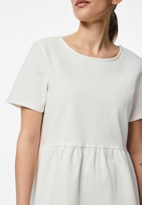 Krämfärgad klänning med kort ärm och rundad halsringning, rynkad midja, mjuk textur och avslappnad passform. Har en enkel design utan dekorationer.