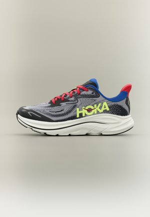 Pelēka un melna skriešanas apava ar sarkaniem šņorēm, zilu un sarkanu polsterētu apkakli, baltu zolīti un spilgti dzeltenu "HOKA" logotipu sānos.