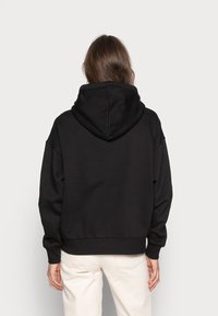 Sudadera con capucha negra de corte relajado, con un dobladillo y puños acanalados, fabricada en una suave tela texturizada. Capucha visible en la parte posterior.