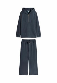 Felpa blu navy con mezza zip, vestibilità oversize e tasca a marsupio, abbinata a pantaloni larghi coordinati con cintura elastica.