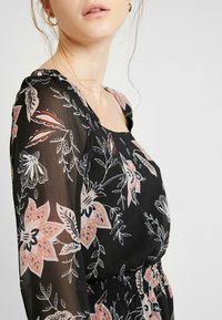 Černé květinové šaty s čtvercovým výstřihem, průhlednými dlouhými rukávy a smockovaným pasem. Květinové vzory v růžové, bíl�é a zelené barvě.