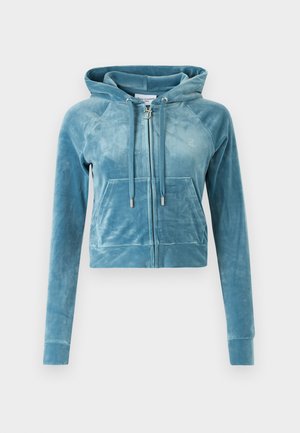 Sagriezta, kapucēta sporta jaka no mīksta zila samta. Iespējas ietver priekšējo rāvējslēdzēju, divas priekšējās kabatas un aizdari kapucei ar sudraba akcentiem.