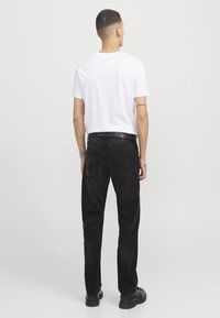 Jeans in denim nero con vestibilità a gamba dritta, abbinati a una t-shirt bianca semplice. L'outfit presenta dettagli minimi e un design classico.