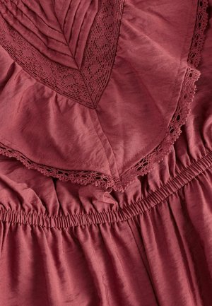 Bordo suknelė su tekstūruotu liemeniu, įrėmintu nėriniais, ir susirinkusia elastine juosta, pagaminta iš švelnios, plazdančios medžiagos.