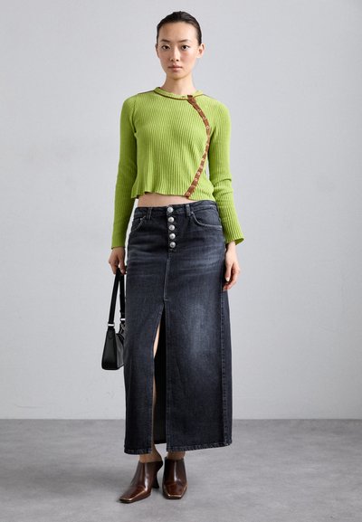 Maglione verde a coste con maniche lunghe e dettaglio dei bottoni laterali, abbinato a una gonna in denim scuro con spacco alto e bottoni argentati, insieme a stivali marroni a punta.