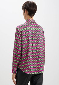 Camicia a maniche lunghe in tessuto rosa con un motivo geometrico di quadrati verdi e bianchi. Include un colletto e polsini con bottoni.