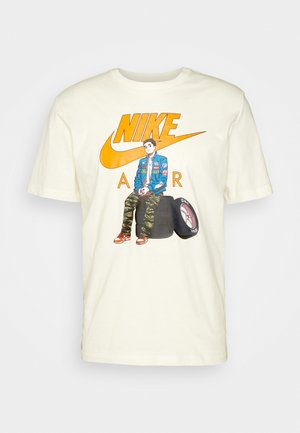 T-shirt en coton crème avec une illustration d'une personne assise sur un pneu, avec un grand logo Nike orange surdimensionné et le texte "AIR".