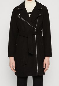Svart ullblandad kappa med bältad midja, asymmetrisk silverdragkedja, breda slag och sidofickor. Slät textur och skräddarsydd passform.