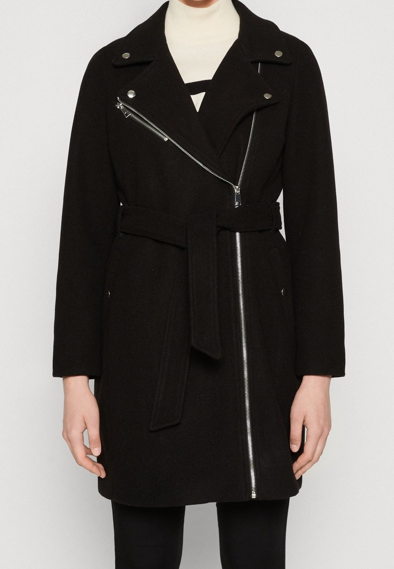 Svart ullblandad kappa med bältad midja, asymmetrisk silverdragkedja, breda slag och sidofickor. Slät textur och skräddarsydd passform.