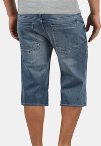 Shorts de mezclilla en azul claro, hasta la rodilla, con cuatro bolsillos, una textura suave y costuras de contraste en los bolsillos traseros.