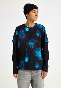 Sort langærmet skjorte med et farverigt blæksprutteprint i blå og teal, parret med grå jeans. Materialet er bomuld med en afslappet pasform.