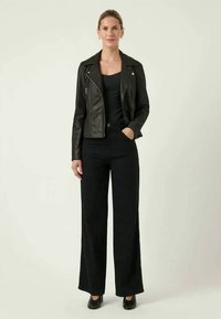 Jaqueta de motoqueiro de couro preta sobre uma blusa preta, combinada com calças largas pretas e saltos pretos. Design simples e ajustado com acentos mínimos.