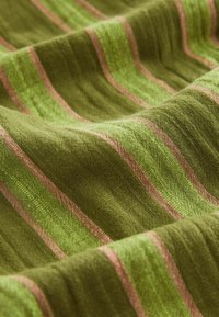 Tissu vert avec motif rayé rose montrant des plis doux et une surface tissée texturée.