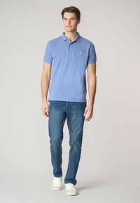 Polo shirt azzurro chiaro con maniche corte, colletto e piccolo logo; abbinato a jeans blu medio e sneakers bianche.