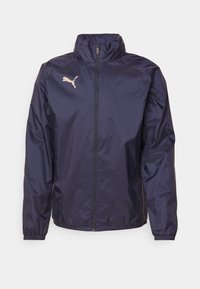 Mørkeblå vindjakke lavet af let, glat materiale; har en høj krave, fuld lynlås og et pink Puma-logo på brystet.