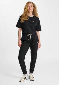 Schwarzes Baumwoll-T-Shirt mit kurzen Ärmeln und kleinem Logo. Kombiniert mit schwarzen Sweatpants, die einen Kordelzug und elastische Bündchen haben.