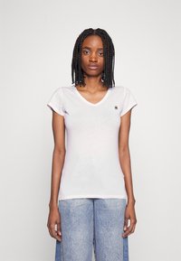 Lichtroze v-hals t-shirt gemaakt van zachte stof met korte mouwen. Voorzien van een klein logo op de borst, gedragen met vervaagde blauwe jeans.