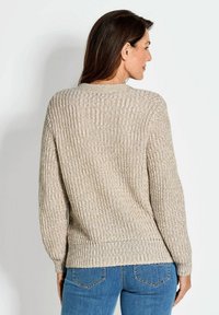 Gebreide trui in beige tinten met een gestructureerd ontwerp, ontspannen pasvorm, geribde manchetten en een brede halslijn, gecombineerd met blauwe jeans.