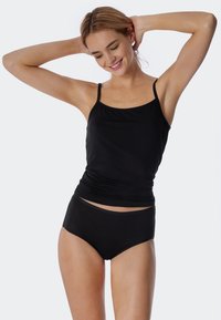 Camisole noire à fines bretelles, associée à un bas noir taille haute. Les deux vêtements ont une texture lisse et un design ajusté.