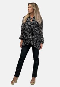 Czarna bluzka w kwiatowy wzór z długimi przezroczystymi rękawami, taliowana, z dekoltem w serek. Zestawiona z eleganckimi czarnymi spodniami i złotymi platformami na obcasie.