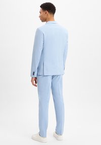 Lichtblauw pak van soepel stof, met een enkelbreasted colbert en op maat gemaakte broek, gecombineerd met witte sneakers.