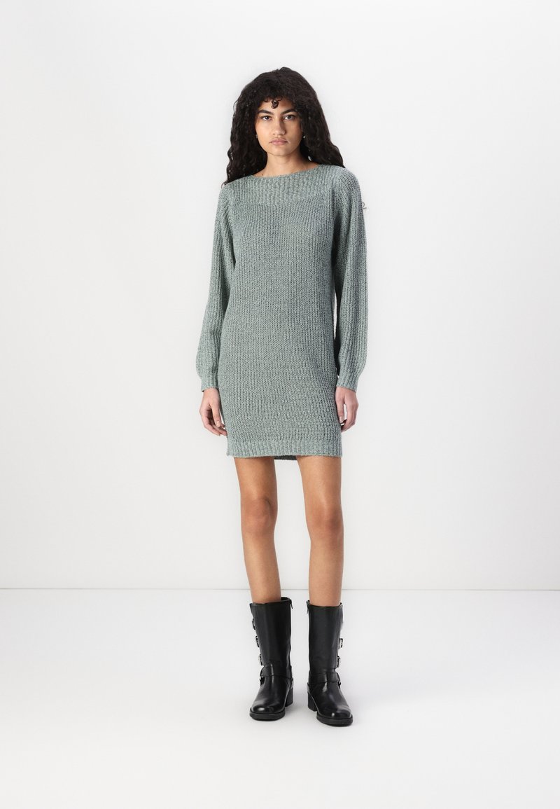 Adīta svārku kleita bālā zaļā krāsā, ar garām piedurknēm un laivu formas kakla izgriezumu. Stilizēta ar ceļgaliem augstām melnām zābakiem. Gluda tekstūra.