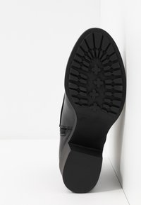 Suela de bota negra con un patrón de goma texturizada, que presenta ranuras y secciones planas para mayor tracción; diseño de cremallera lateral visible en la parte superior.